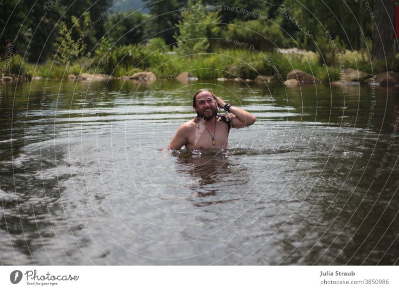 Long haired man bathes in a natural lake in summer Summer vacation Nature Swimming lake Lake Water long hairs Beard Chain Bracelet Smiling naturally Lakeside