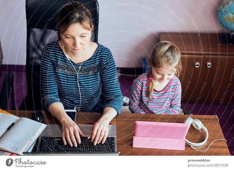 Woman mother working doing her job remotely during video chat call stream online course webinar on laptop from home while her daughter watching video on tablet