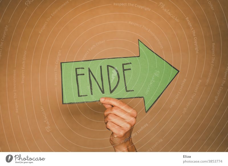 Hand holds a green arrow with the word end written on it. Separation, off, over. End Divide from Transience Green Past sign Arrow Direction Orientation