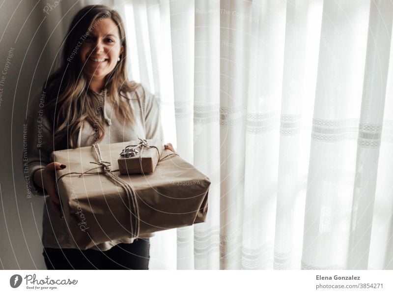 Young woman holds in hands stacked Christmas gift boxes in craft paper with juniper. Christmas presents concept. christmas merry christmas new year women