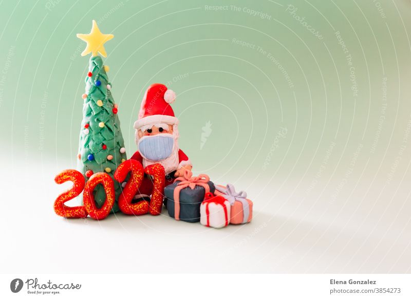 Playful clay christmas concept. Colorful handmade miniature Christmas tree, presents and Santa Claus with mask on green background. 2021 new year.