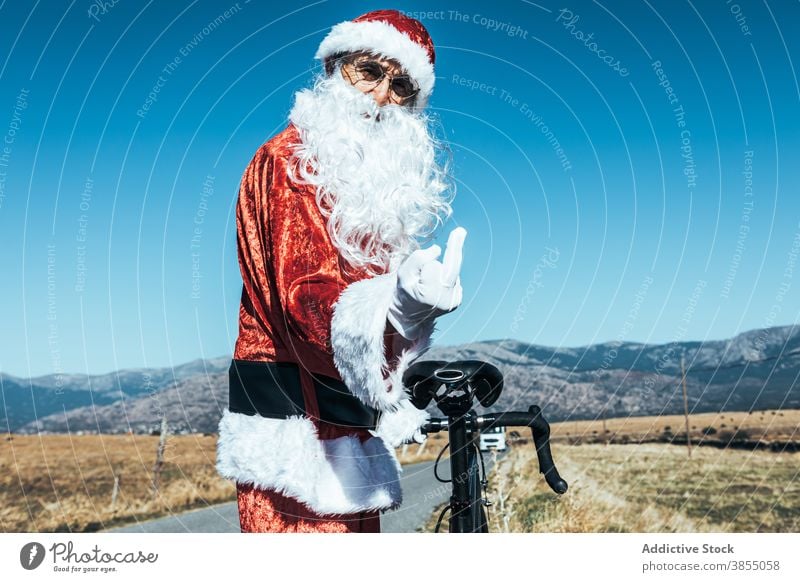 Rude Santa Claus showing middle finger fuck santa claus rude gesture bicycle road santa hat rebel expressive male stand rural roadway bike sunny mature senior