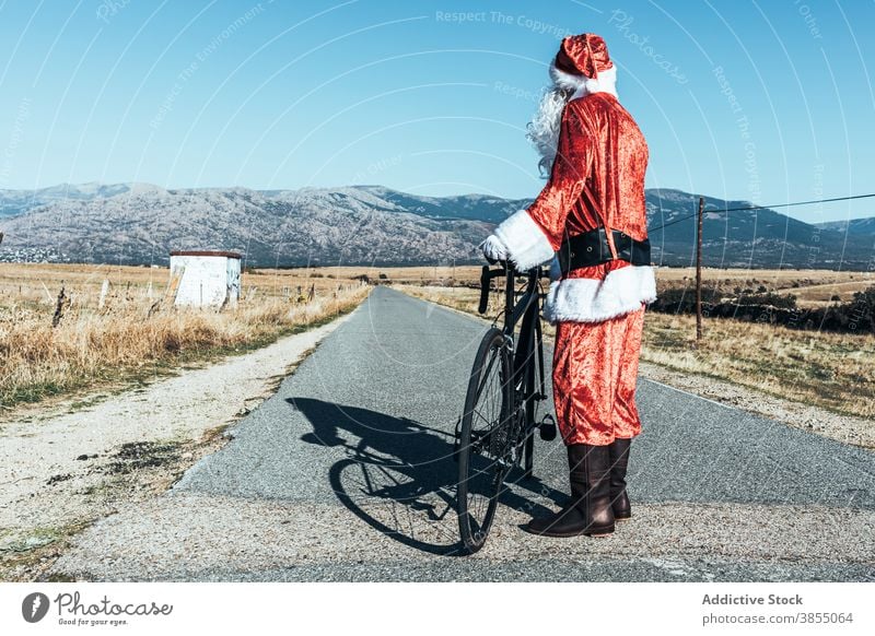 Anonymous Santa Claus near bicycle on road in countryside santa claus relax roadway vehicle bike santa hat male beard costume red color modern style stand