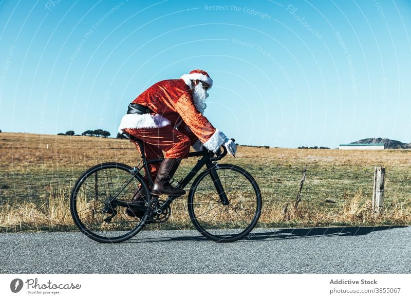 Santa Claus riding bicycle along mountain road santa claus ride bike empty costume red color male modern journey freedom speed trip move sunny activity