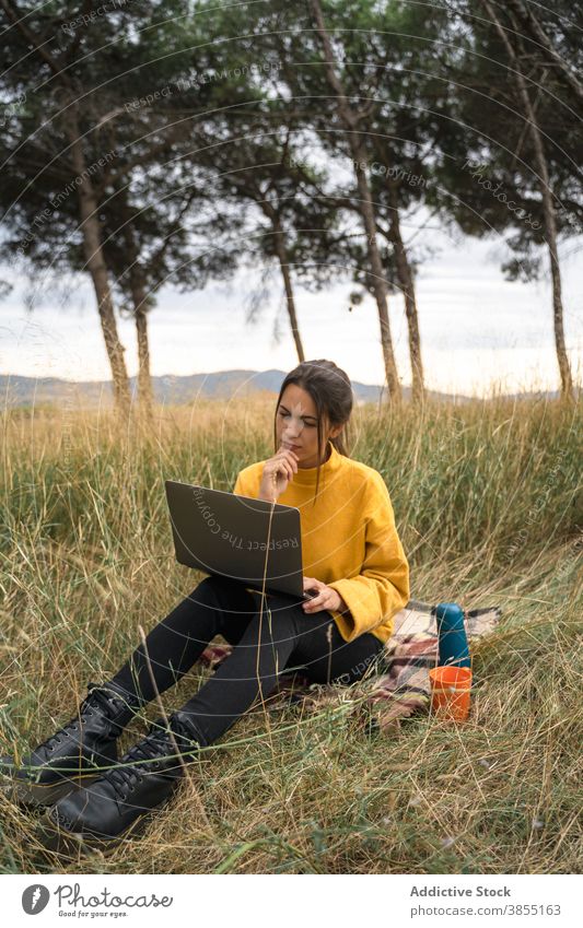 Thoughtful woman working on laptop in meadow freelance remote field countryside project autumn female blanket job internet pensive gadget computer busy watch