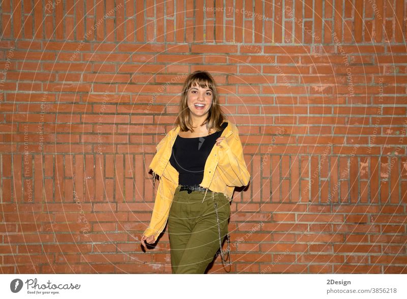 Beautiful young woman stands near an old brick wall in the city at night standing attractive smiling happy casual attire female person beautiful lifestyle