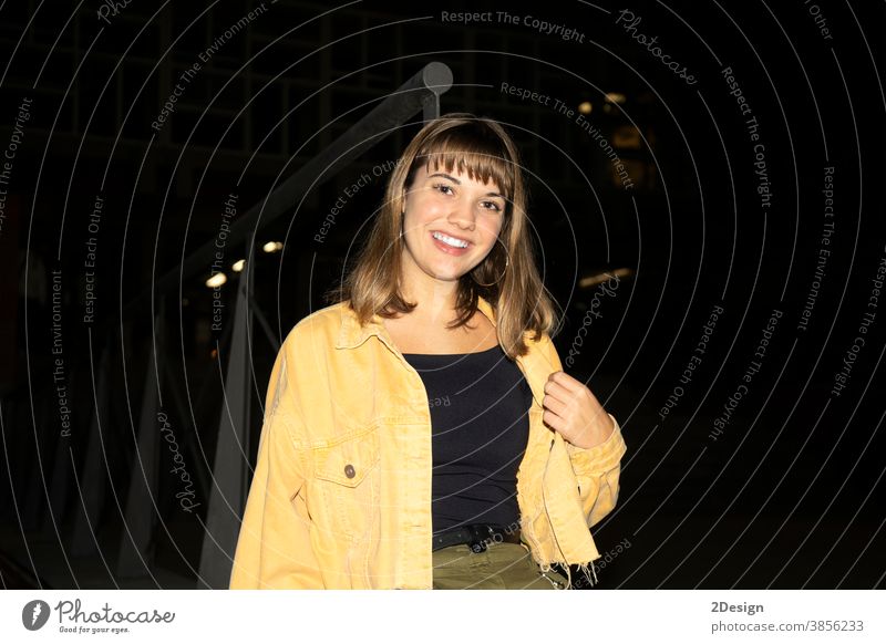 Young beautiful girl sitting in a bench in a public city park at night while looking to camera young female 1 attractive pretty happy outdoor woman person