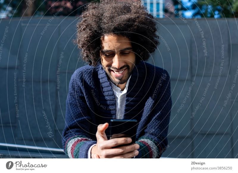 Smiling African American guy writes SMS to friends on phone. man 1 afro mobile smiling happy male technology mobile phone message black african outdoor portrait