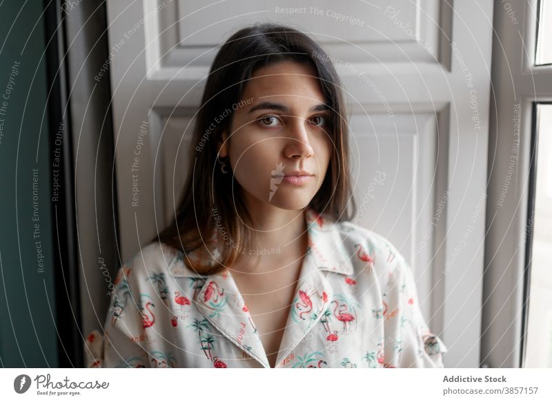 Thoughtful woman looking at camera thoughtful window contemplate smile dreamy casual stand observe carefree female modern young enjoy apparel brunette attire