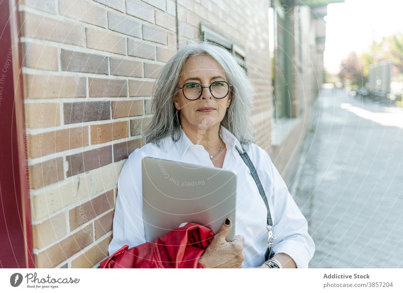 Mature businesswoman with laptop standing on the street in the city entrepreneur middle age nature determine style female gadget device confident modern manager