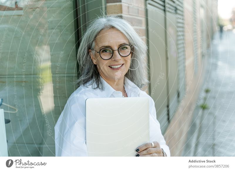 Mature businesswoman with laptop standing on the street in the city entrepreneur middle age nature determine style female gadget device confident modern manager