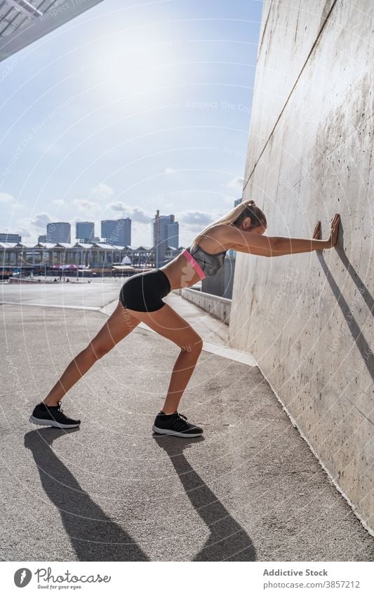 Sportswoman stretching legs near wall of building sportswoman lean exercise warm up active training city female athlete fitness sportswear healthy body young