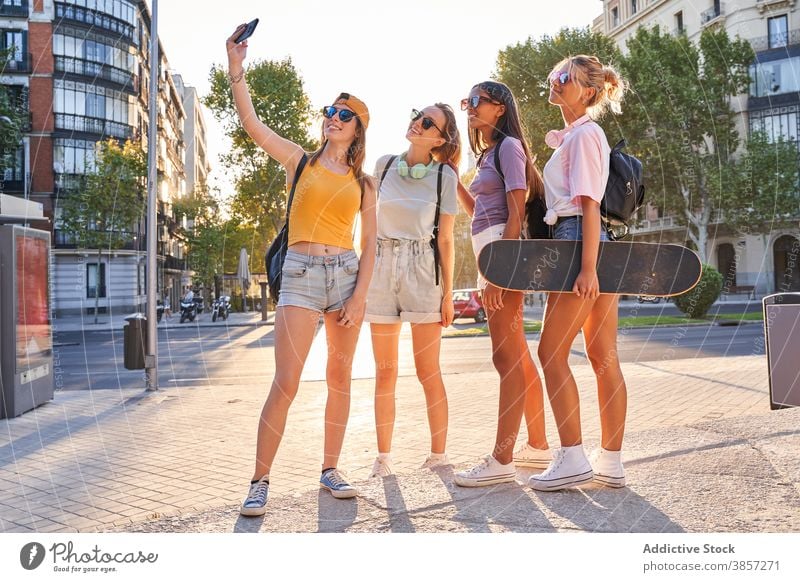 Positive female teenagers taking selfie in city girlfriend urban summer happy trendy cheerful together group skateboard active phone mobile street diverse