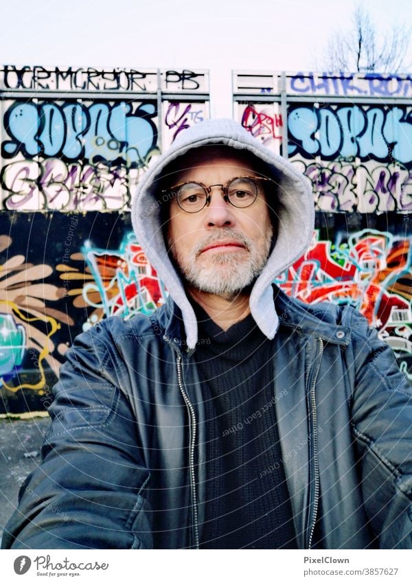 Old graffiti fan in front of a graffiti wall Graffiti Man Human being Wall (barrier) Masculine Adults street art urban City Face Eyeglasses Hooded (clothing)