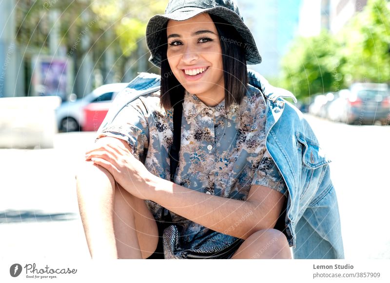 Portrait of a brunette Latina woman with hat, looking into the camera and holding her arm in one hand latin american woman portrait urban background person