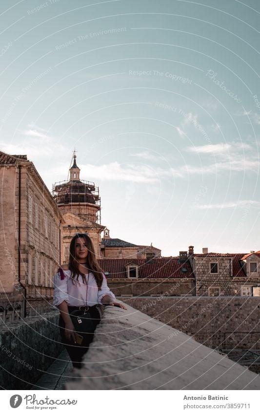 Moody vertical portrait of a brunette standing at the walls of Dubrovnik city vacation famous medieval lifestyle stone beach panoramic pose covid modern leather