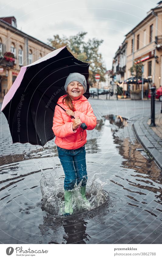 Little girl holding big umbrella jumping in the puddle on rainy gloomy autumn day raining outdoors little seasonal fall childhood beautiful weather outside kid