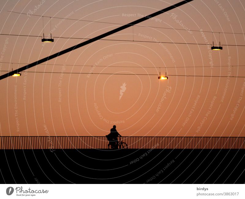 Cyclists ride over an illuminated bridge at dawn. Way to work Cycling cyclist Bridge Street lighting Twilight clearer on one's own Sunset Dusk Light Lighting