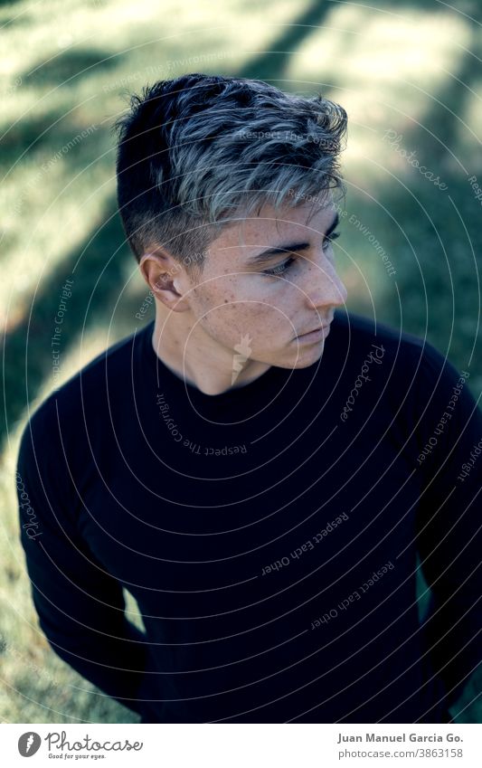 Teenage boy with a serious expression and dyed hair with highlights, wearing a tight black T-shirt that defines his athletic body 14-15 years hairstyle