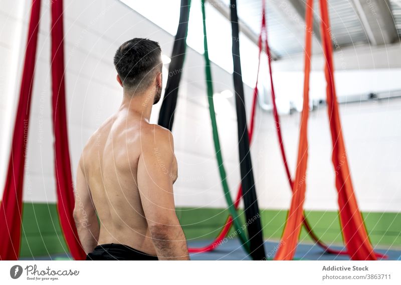 Anonymous male dancer examining aerial silks man studio rehearsal gymnastic examine colorful shirtless cloth fabric practice skill professional perform talent