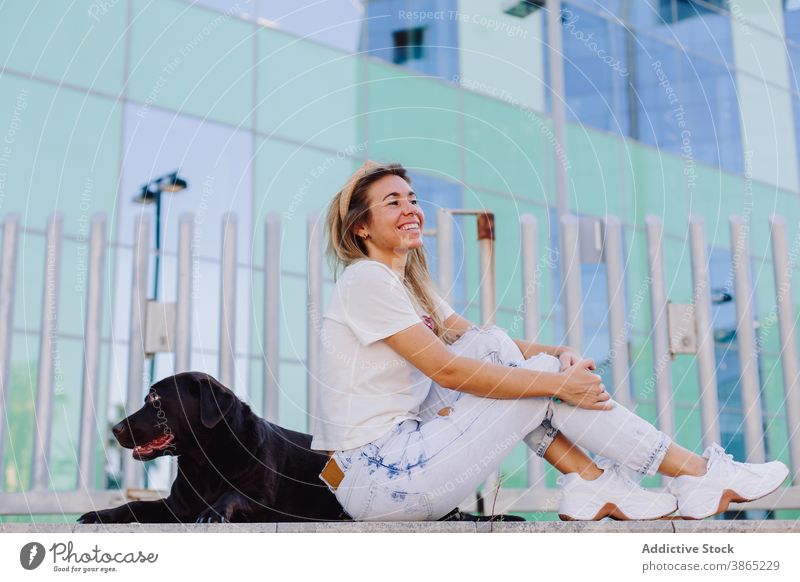 Cheerful woman with black dog in city friendship obedient labrador retriever relax bench summer animal female pet domestic together stroll sit companion smile