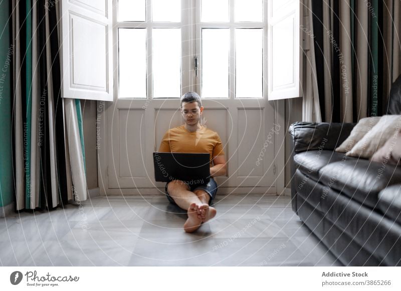 Busy man working on laptop in living room freelance remote home typing project concentrate browsing male casual outfit floor sit window legs crossed device job