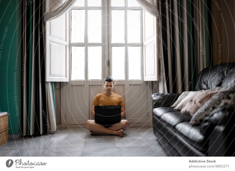 Busy man working on laptop in living room freelance remote home typing project concentrate browsing male casual outfit floor sit window legs crossed device job