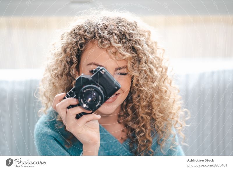 Cheerful woman with photo camera at home photographer take photo cheerful talent cozy photography curly hair female bright apartment casual charming gadget