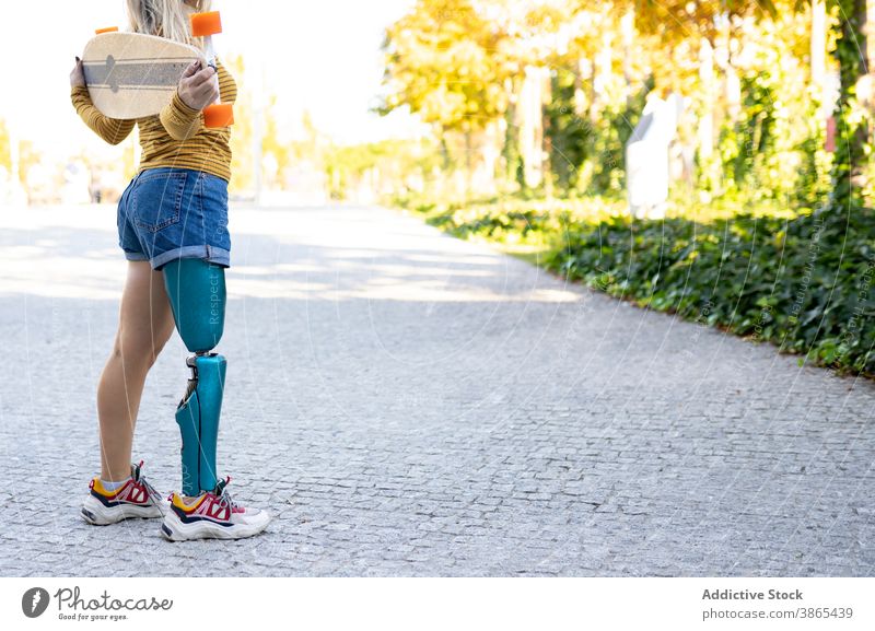 Slim woman with longboard and leg prosthesis on street bionic skater artificial limb disable urban female skateboard town modern sunlight sunny amputee summer