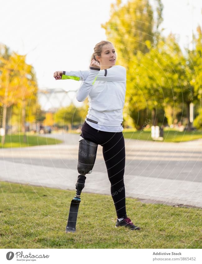 Sportswoman with leg prosthesis warming up in park runner paralympic warm up sportswoman training forward bend exercise female artificial limb amputation bionic