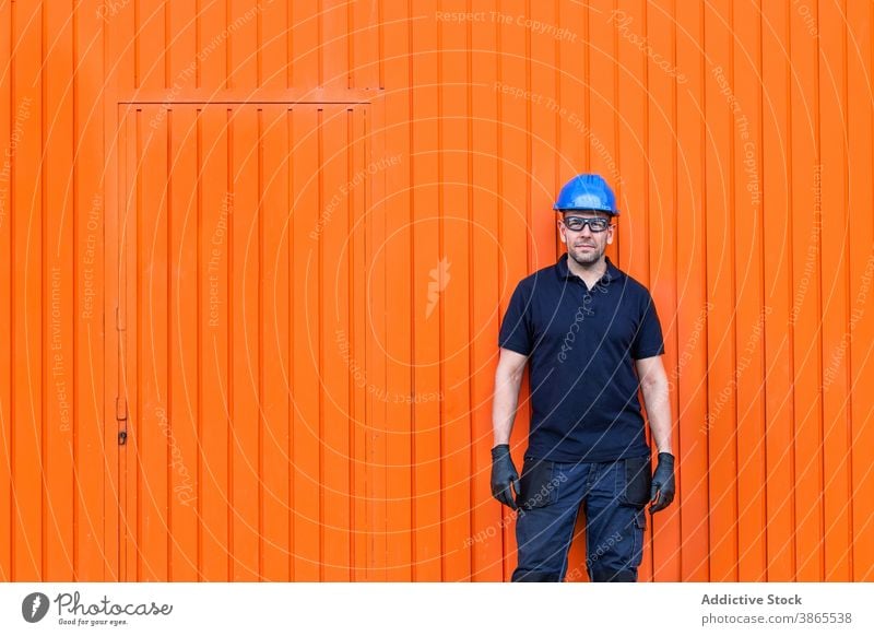 Male worker in hardhat standing near workshop cheerful confident friendly man professional mechanic positive wall adult male workman bright smile job happy