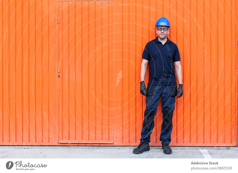 Male worker in hardhat standing near workshop cheerful confident friendly man professional mechanic positive wall adult male workman bright smile job happy