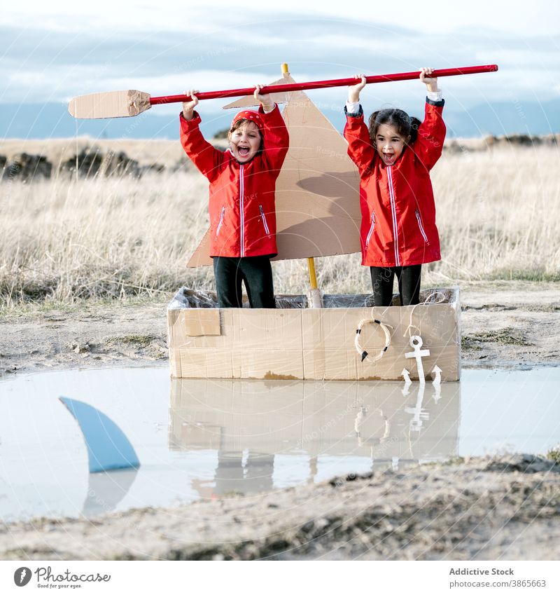 Excited girls playing in cardboard boat in countryside having fun carton child together inspiration paddle game creative imagination handmade cheerful happy