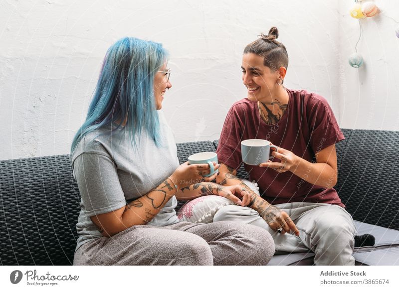 Happy girlfriends enjoying hot drinks on sofa women smile rest couple lesbian mug home cozy informal rebel alternative lgbt homosexual same sex couch together