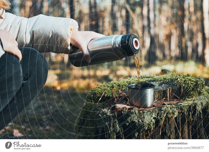 Women having break during autumn trip pouring a hot drink from thermos flask on autumn cold day. Active women wandering in a forest actively spending time