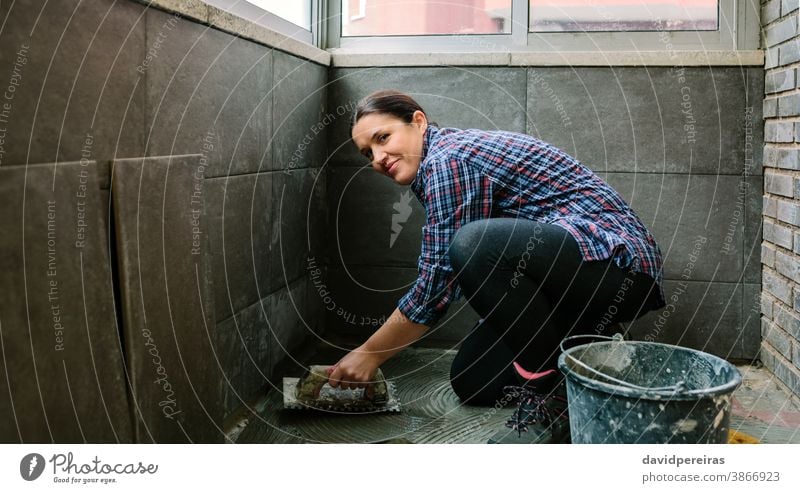 Female mason laying a new tile floor woman masonry builder looking camera smiling tiling reform maintenance tiler glazed terrace working manual worker handyman