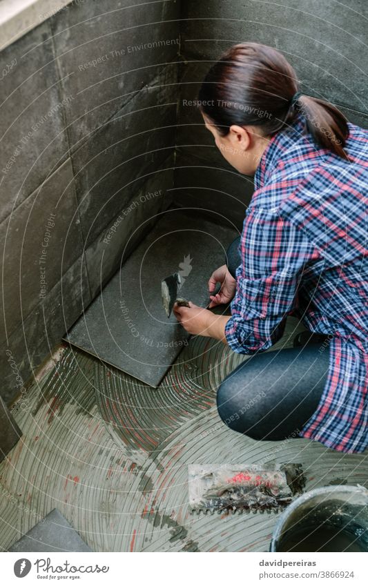 Female manual worker laying a new tile floor top view mason woman reform light knocks spatula tap glazed terrace female handyman placing diy overhead