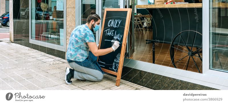 Restaurant owner writing on a blackboard only takeaway waiter coronavirus face mask restaurant safe food banner web header panorama panoramic business apron