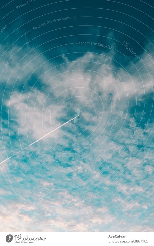 Plane flying on the sky between the clouds in a minimalistic image with a saturated blue color plane trail smoke silhouette speed trace aeroplane jet show tail