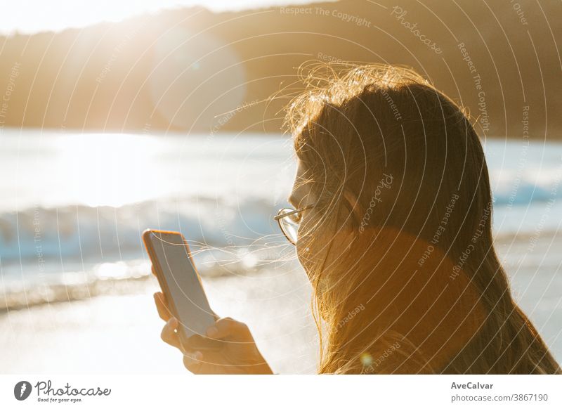 Young woman checking his cellphone in the beach during a sunset with copy space on colorful tones person smiling wireless holding technology internet laughing