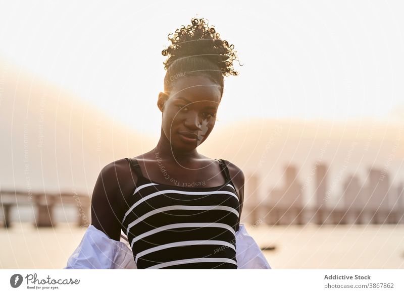 Calm black woman standing on city embankment at sunset sea tranquil pensive relax calm sunlight urban young female african american ethnic seafront thoughtful