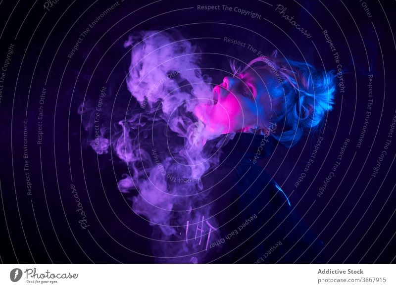 Expressive woman smoking in dark studio vape smoke e cigarette neon light steam cool female style nicotine smoker habit confident young bad unhealthy addict