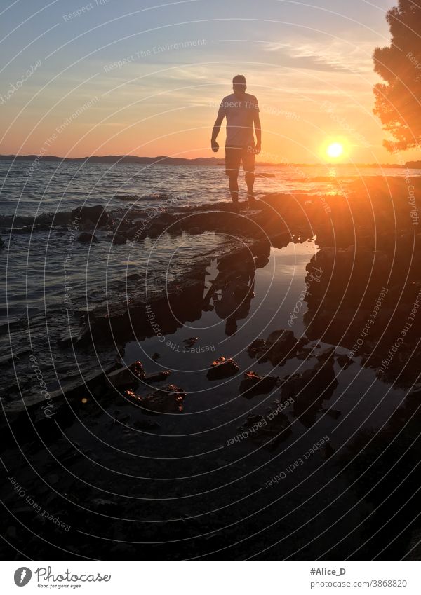 Man silhouette in the sunset while walking on rocky beach dark body tranquility seascape dawn sundown idyllic boy Orange twilight beautiful coastline adult