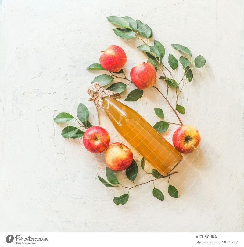 Composing with homemade apple juice in glass bottle with apples and green leaves on white background. Top view homemade food apple tree twigs pattern top view