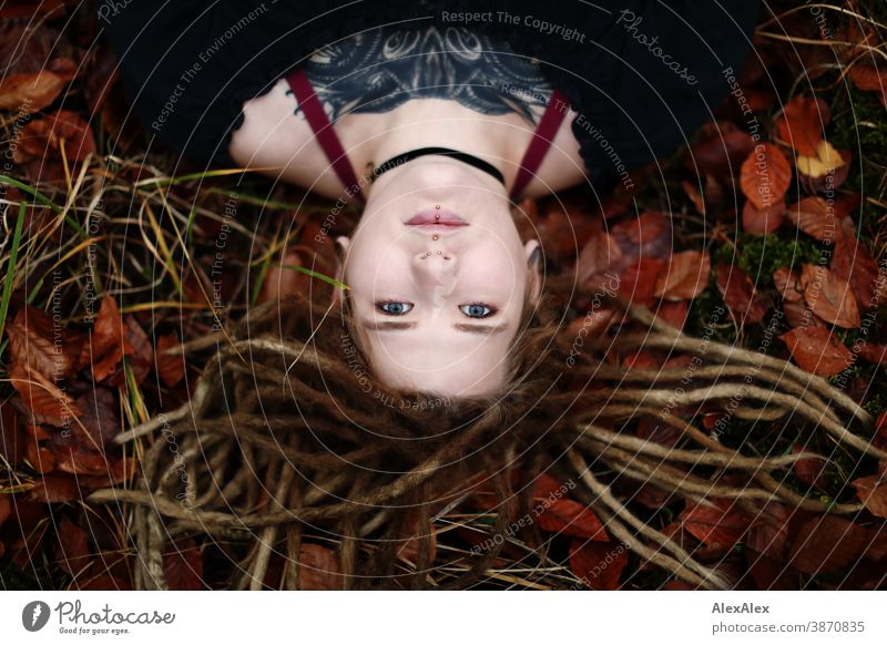 Portrait of a young woman with dreadlocks and tattoos, lying in the wood Woman Dirty Blonde tattooing Jewellery Piercing earring Concealed Direct Nahe Skin