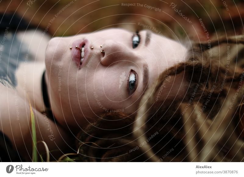 Lateral portrait of a young woman with dreadlocks and tattoos, lying in the wood Woman Dirty Blonde tattooing Jewellery Piercing earring Concealed Direct Nahe