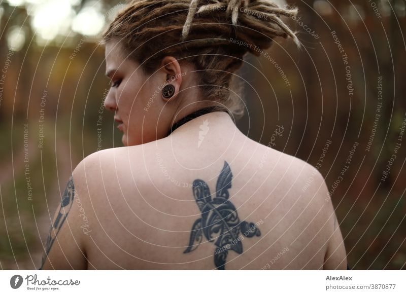 Portrait of a young woman with dreadlocks and tattoos in the forest Woman Dirty Blonde tattooing Jewellery Piercing earring Upper body Naked Concealed Direct