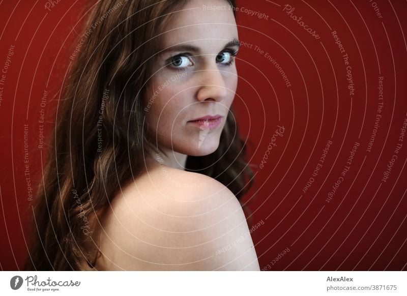 Lateral portrait of a young woman in front of a red wall Woman Slim pretty Brunette long hairs Shoulder Face smart emotionally Skin see look Looking Direct