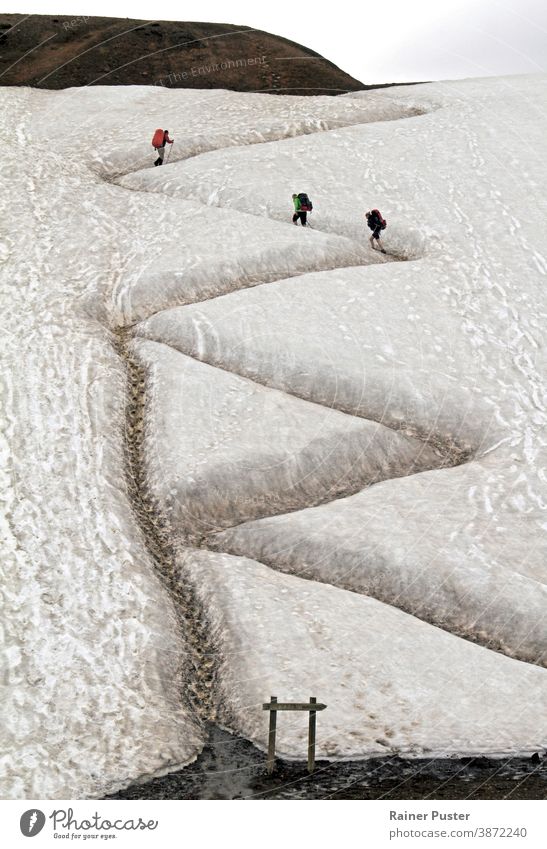 Three hikers on a winding path in Iceland with traces of a shortcut taken by other hikers serpentine road zig zag concept upward activity adventure backpack