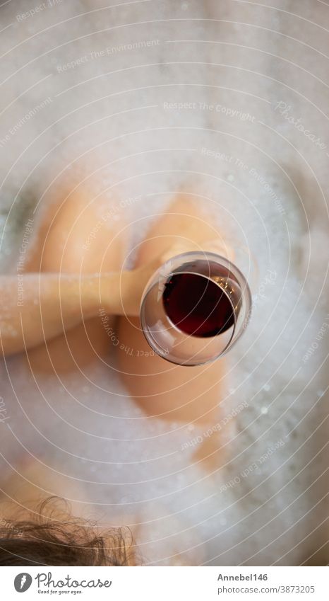 Young woman's hand holding wine glass in bathtub, drinking red wine and lying in bathtub with bubble foam, top view, relaxtion and spa concept bathroom young